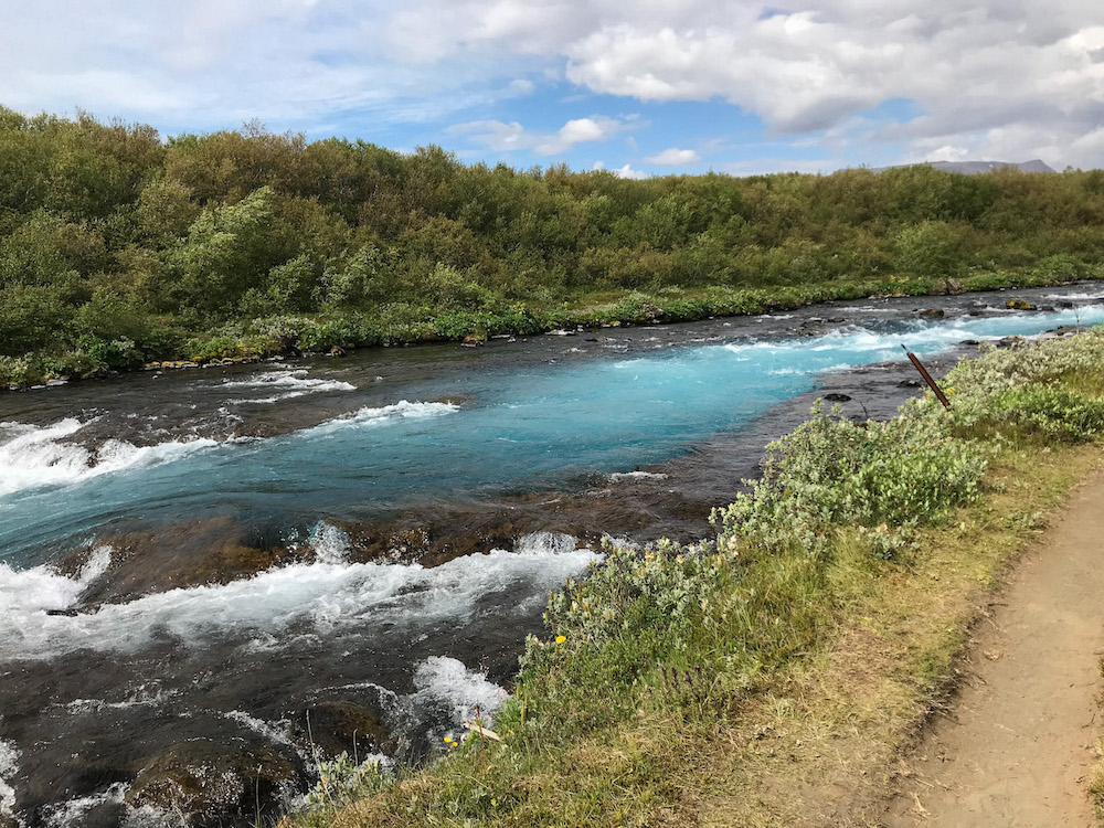 Fluss mit türkisfarbenem Wasser, grüne Büsche am Rand