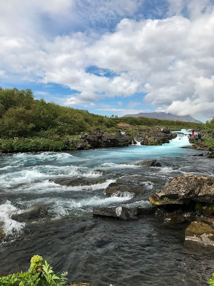 Fluss mit türkisfarbenem Wasser, im Hintergrund ein kleiner Wasserfall