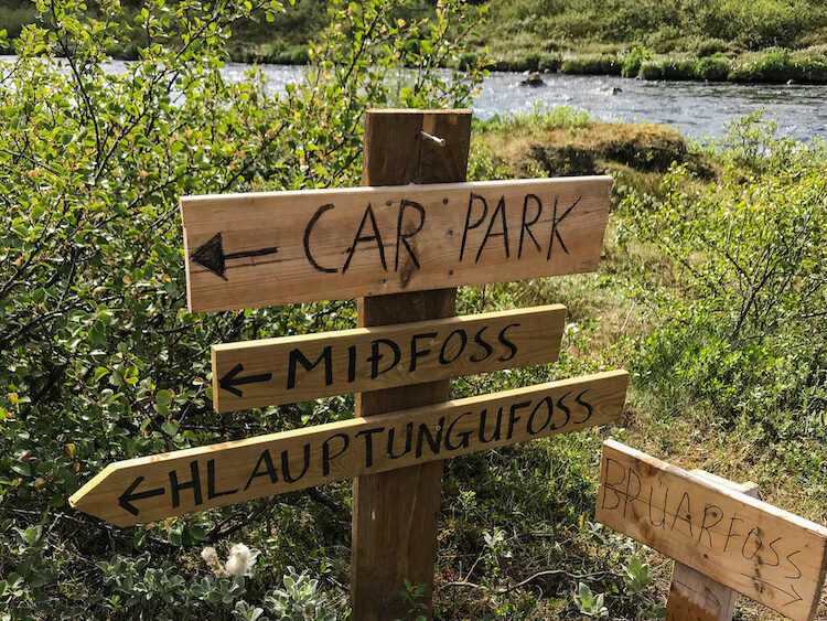 Ein Holzschild zeigt den Weg zu den Wasserfällen Bruarfoss, Midfoss und Hlauptungufoss und dem Parkplatz.