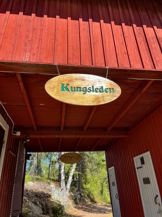 Holztafel, die den Wanderweg Kungsleden ausweist an einem roten Holzhaus