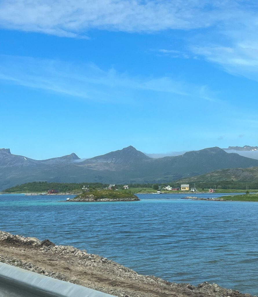 Ausblick in den Fjord mit türkisfarbenem Meer, ein Berg und blauer Himmel im Hintergrund