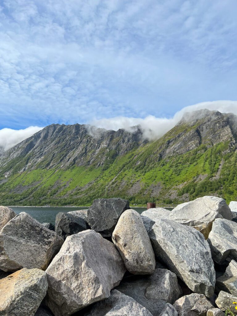 Sehr große graue Steine im Vordergrund, dahinter der Fjord mit hohen Bergwipfeln, die in Wolken hängen