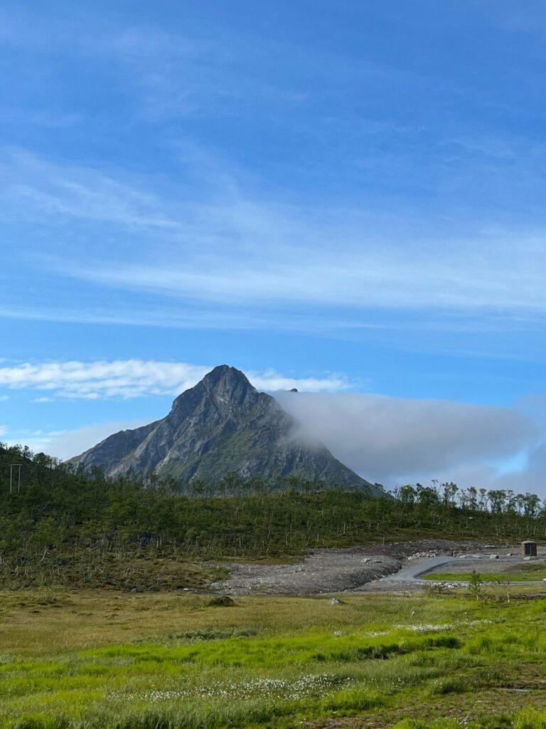 Spitzer Berg in Wolke, davor flache Ebene mit kleinen grünen Bäumen