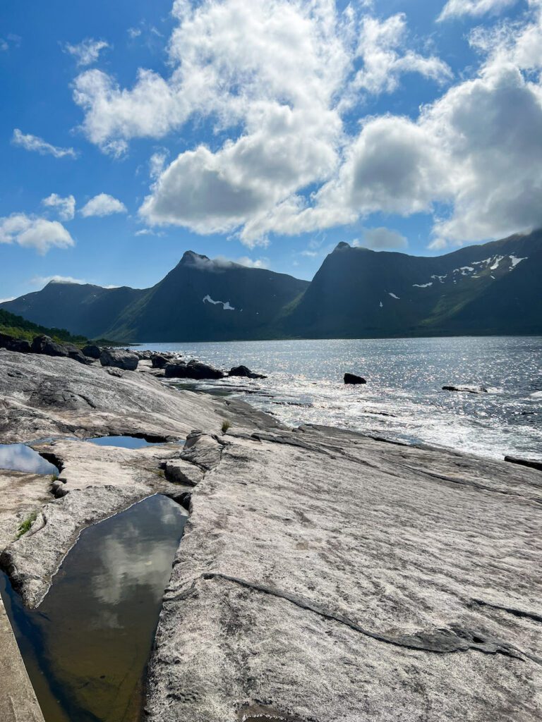 Flache Steine am Boden, dahinter ein Fjord mit hohen Berggipfeln