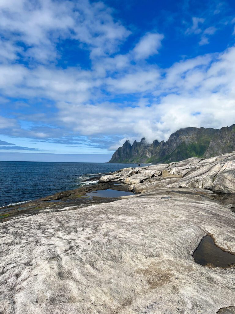 steiniger Untergrund führt entlang des Fjords zum Ausblick auf Berggipfel