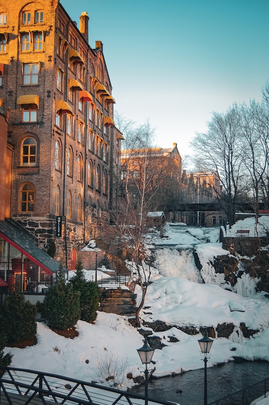 Hohe Backsteingebäude entlang eines Flusses in winterlicher Landschaft